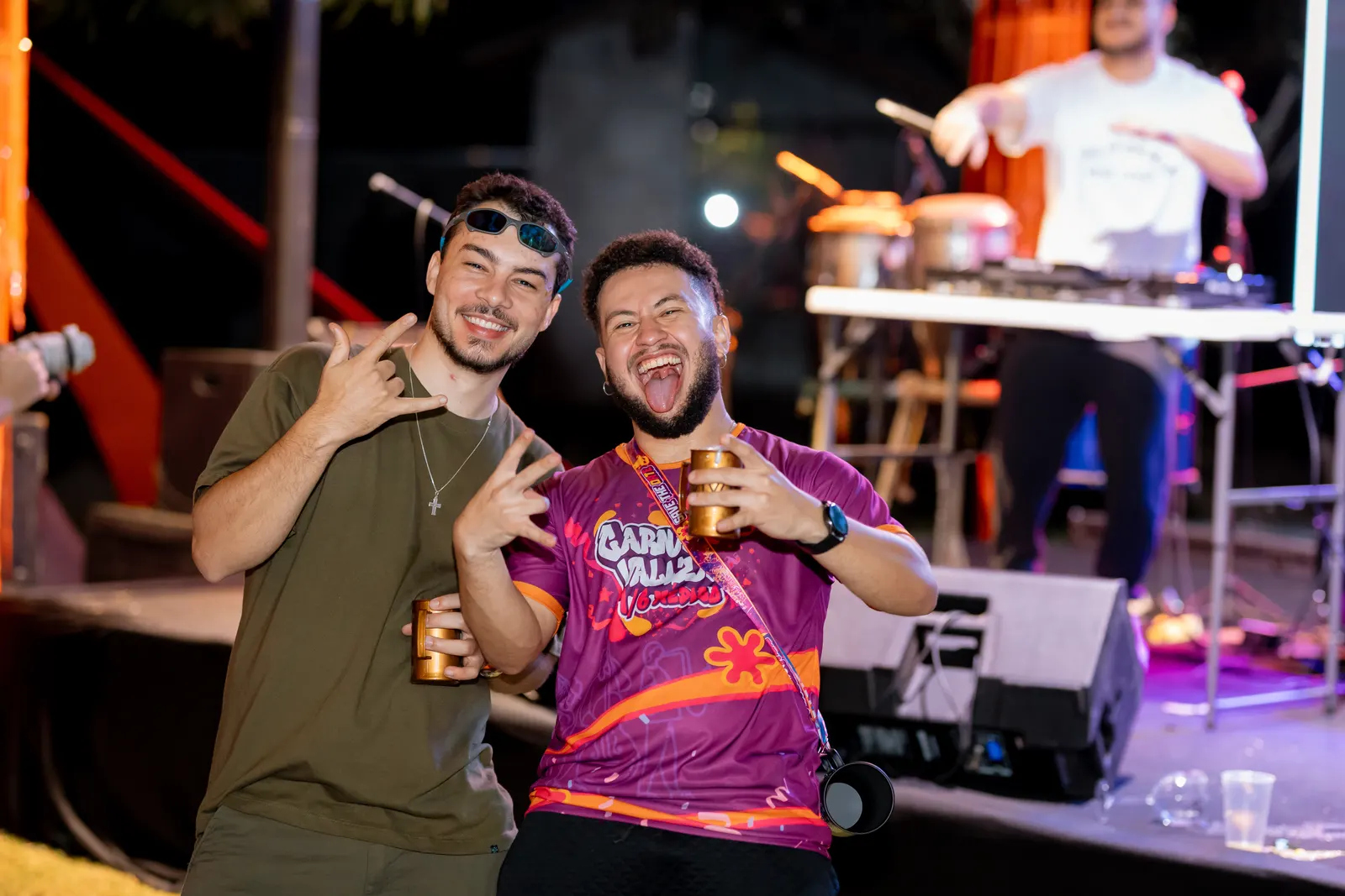 Dois formandos sorrindo em frente à cabine do DJ, um deles com a camisa da festa Carnavalizza.