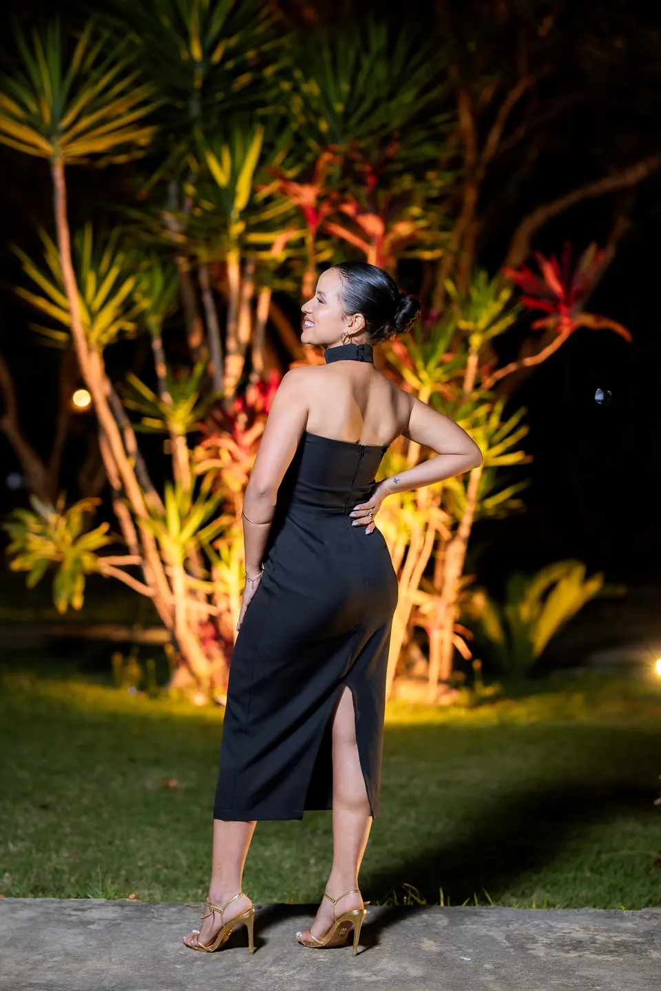 Formanda de costas mostrando o decote do vestido preto em retrato noturno no jardim.