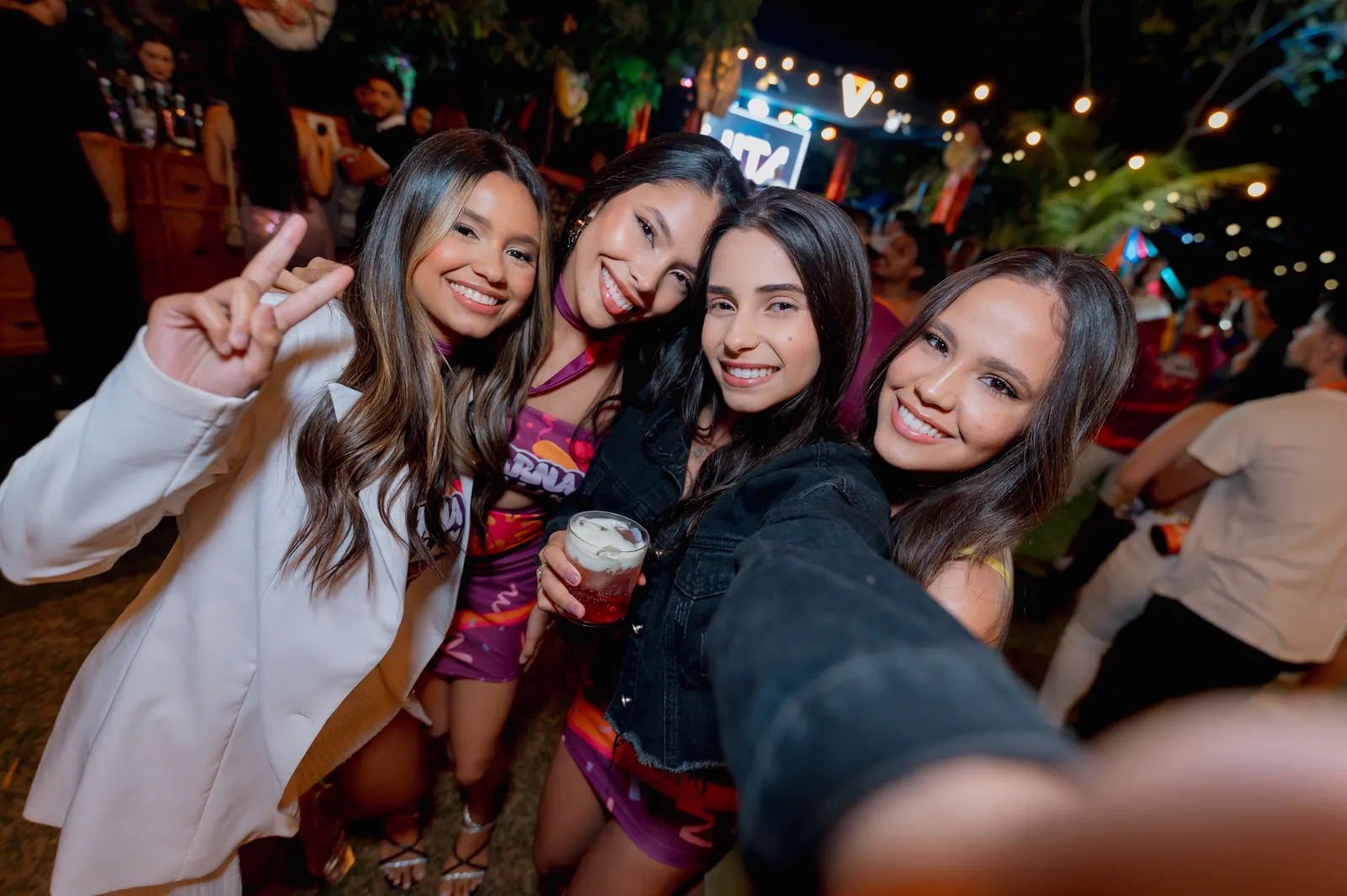 Quatro formandas fazendo selfie e sinal de paz na festa ao ar livre.