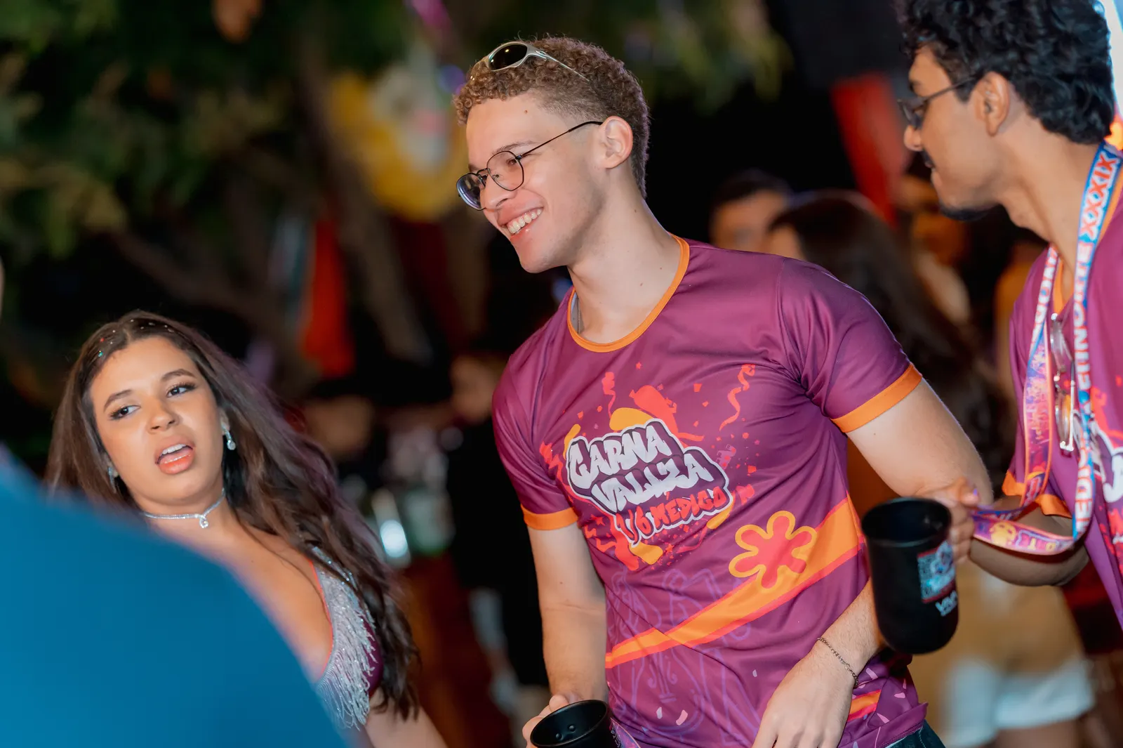 Formando de óculos com a camisa da festa rindo ao lado de uma colega na pista.