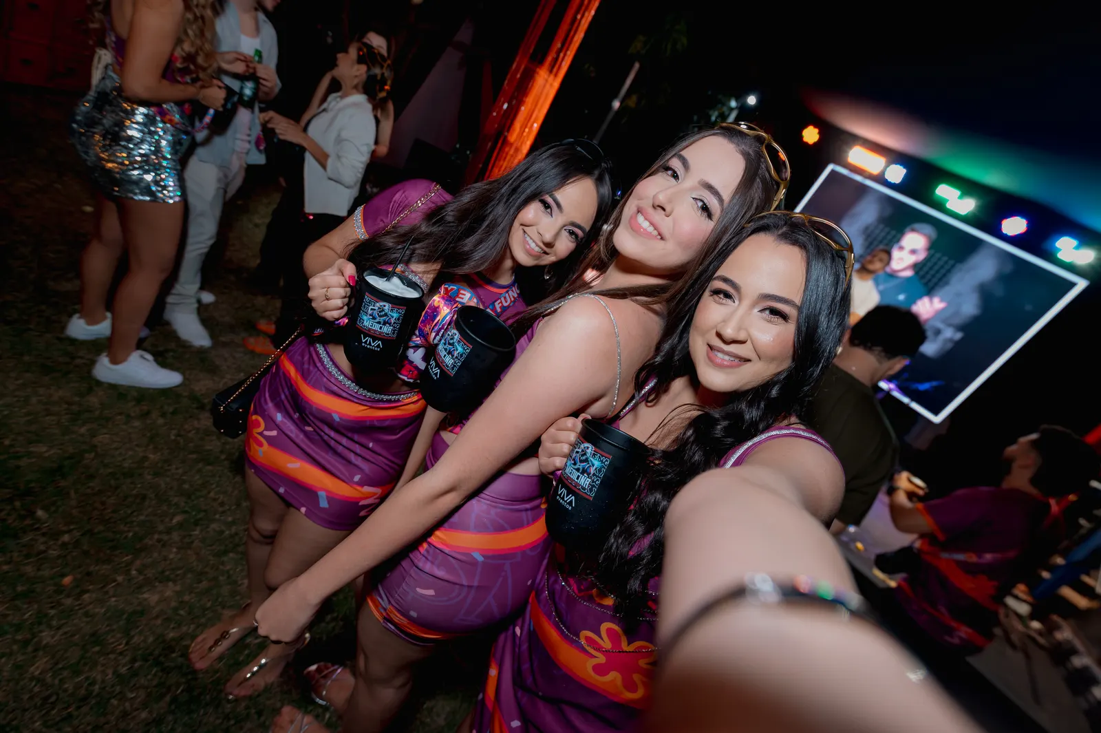 Formandas com a roupa da festa tirando selfie juntas perto do telão.